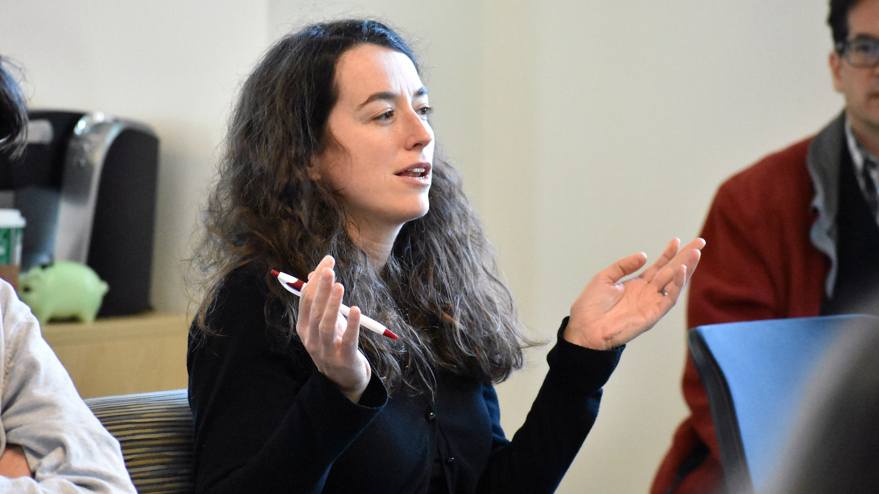 Professor Ellen Lau, seen in profile sitting in an audience after a lunch talk, asking a question, with palms up at shoulder height in an interrogative posture