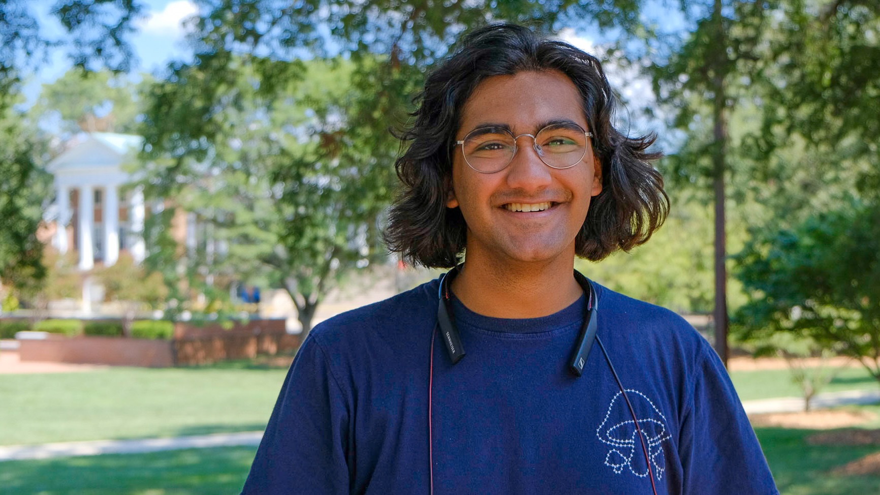 Mal Shah, PhD student in Linguistics, standing outside under oak trees on McKeldin Mall.