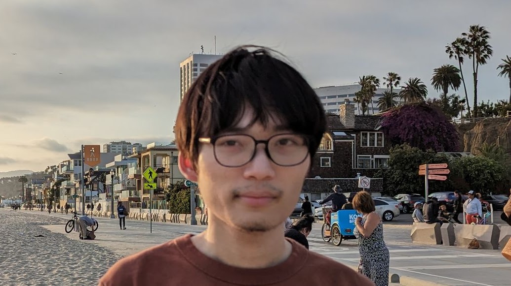 A young man in glasses, standing on a Californian beach: it's Philosophy PhD student, Yunhui Bai!