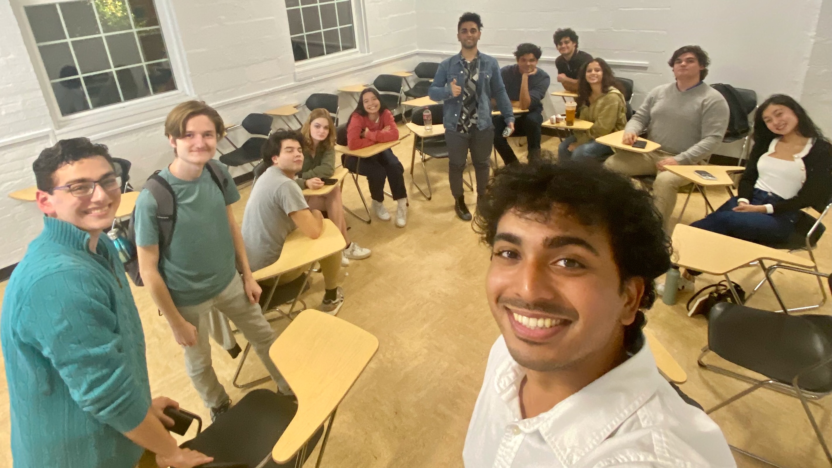 A group of undergraduate students in a club meeting, smiling for a group selfie.