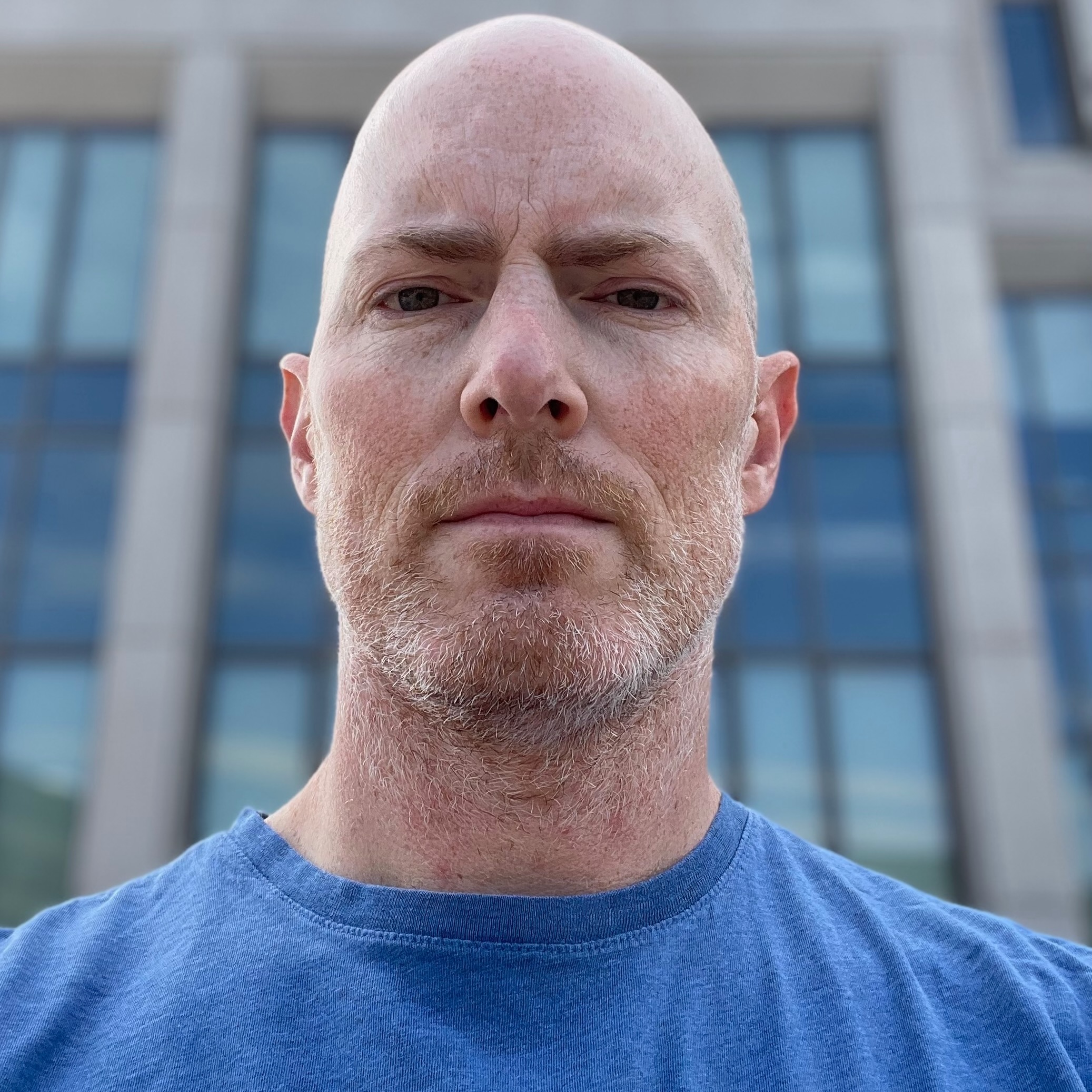 Close portrait of a man with a stern expression and military bearing, wearing a blue t-shirt.