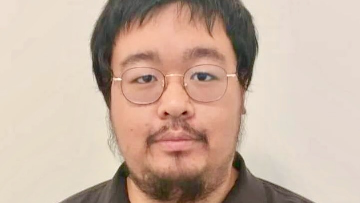 Close portrait of a young man's face, with a beard and round glasses.