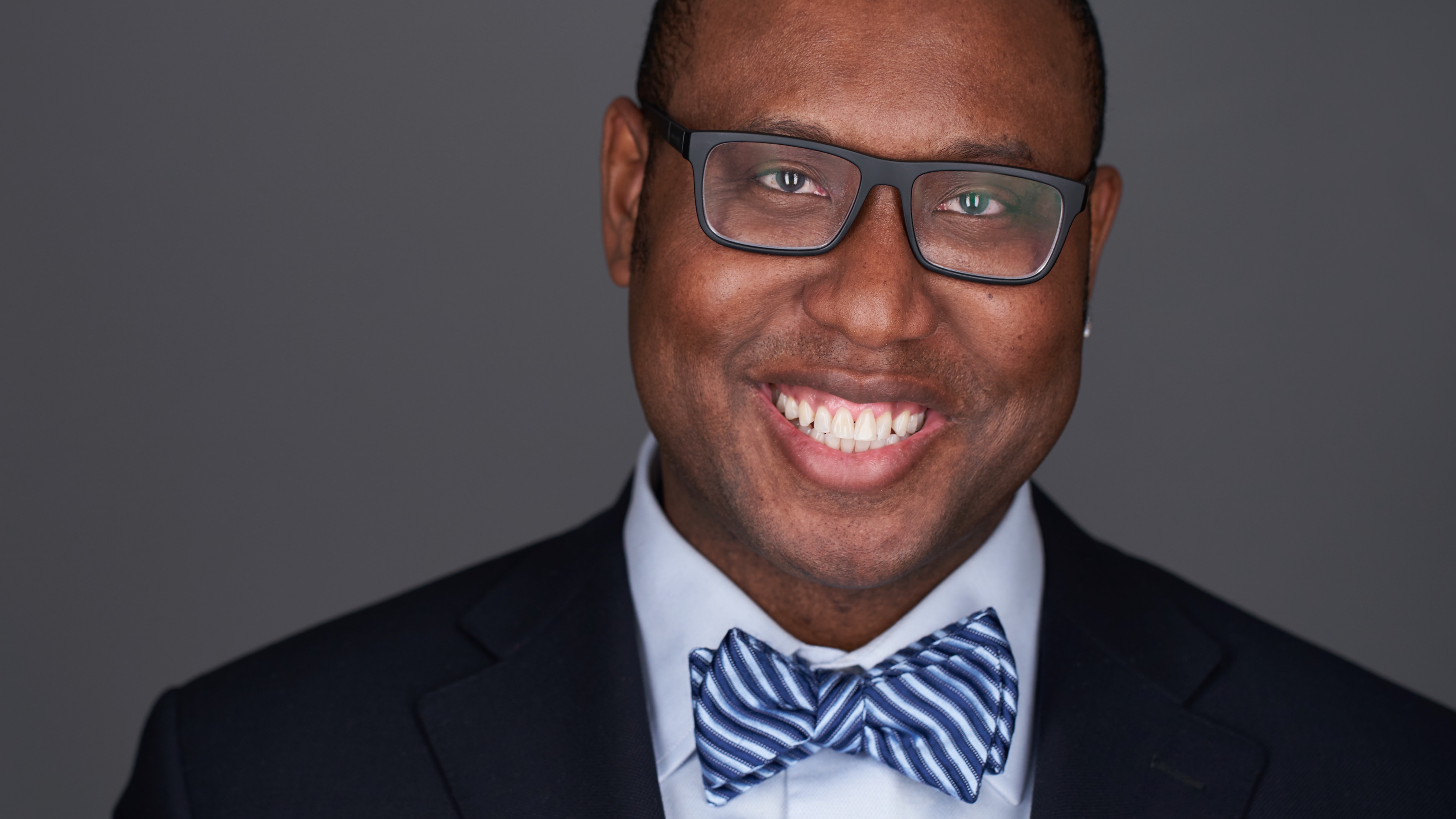 Professional photo of a man in a dark blue jacket with a light blue bow tie.