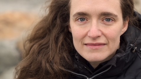 Close portrait of a woman outside, with long brown hair.