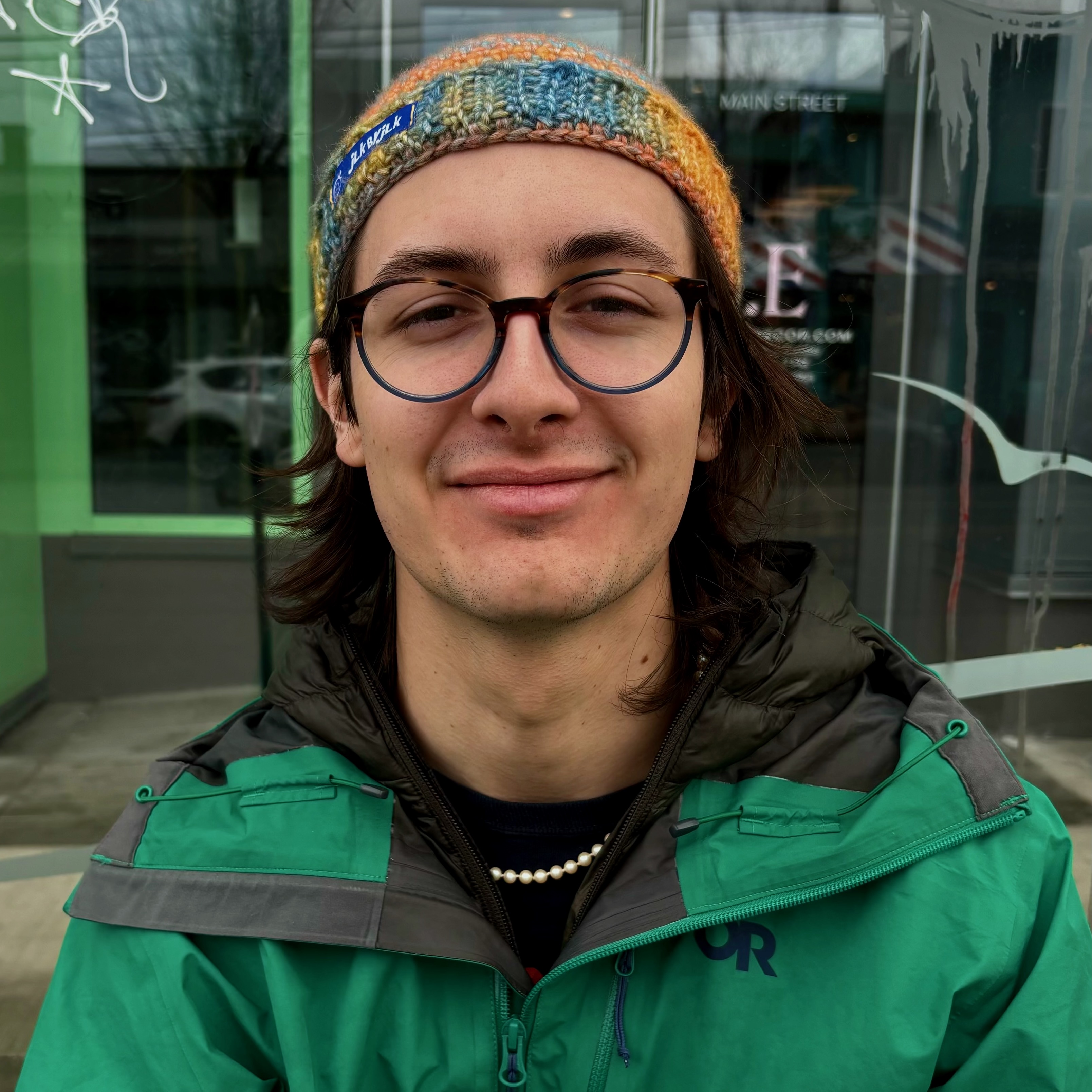 Close portrait of a young man's face - he is outside wearing a green raincoat.