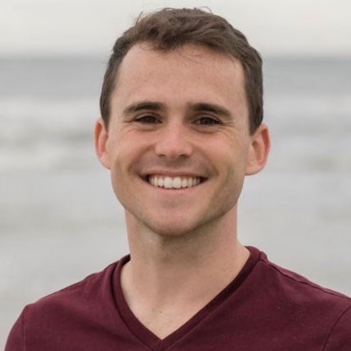 A man smiling, standing on the beach.