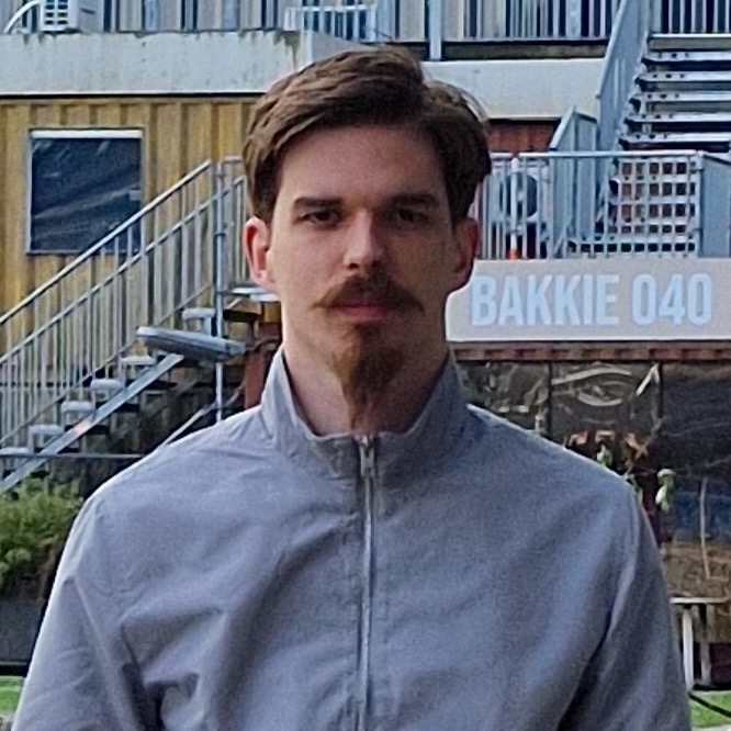 A young man standing outside in a courtyard looking firmly at the camera.