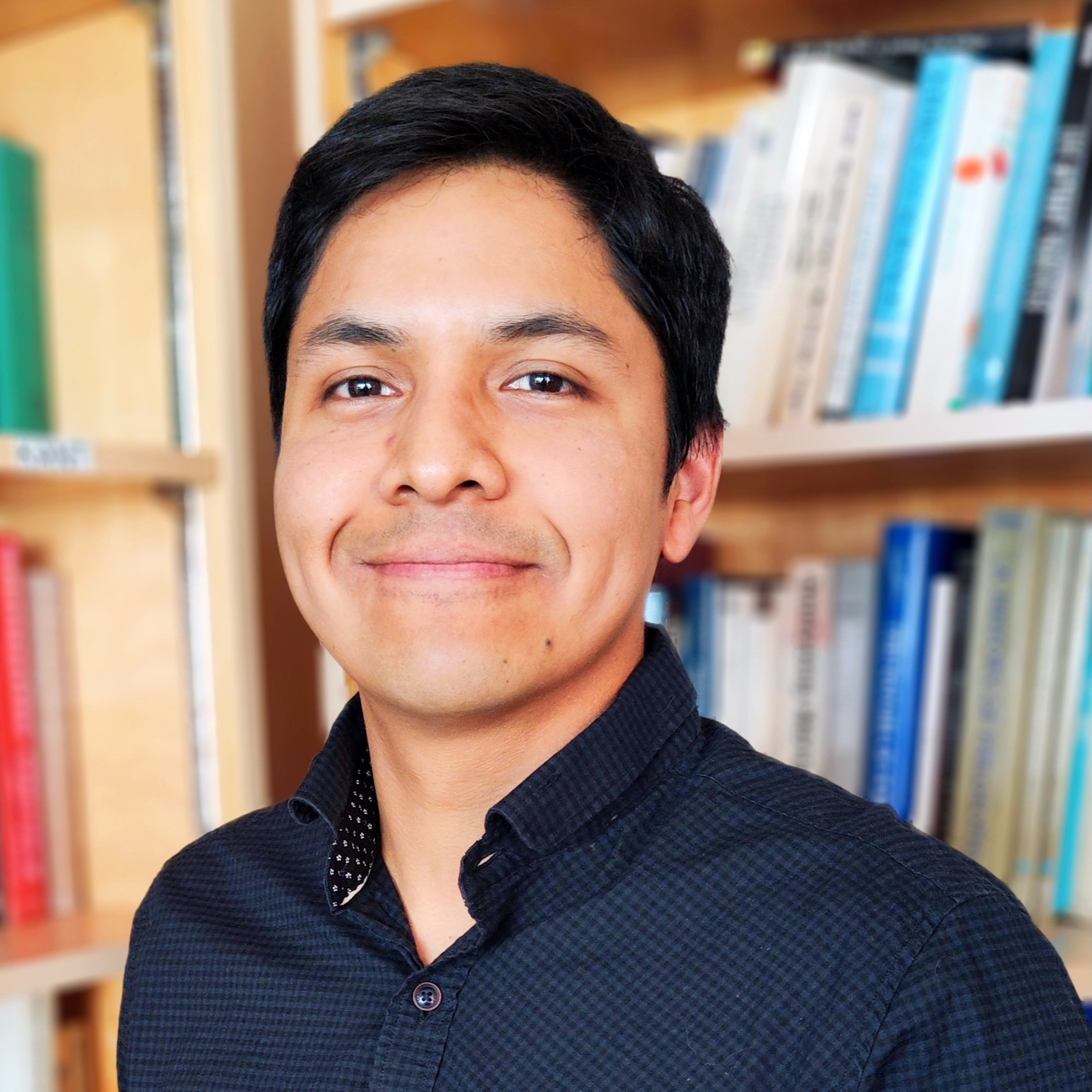 A young man standing in front of full bookcases, smiling.